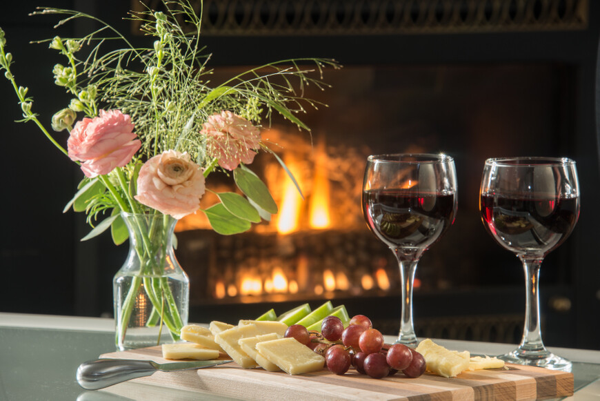 cheese plate, a glass of wine, and flowers on a table in front of a fireplace